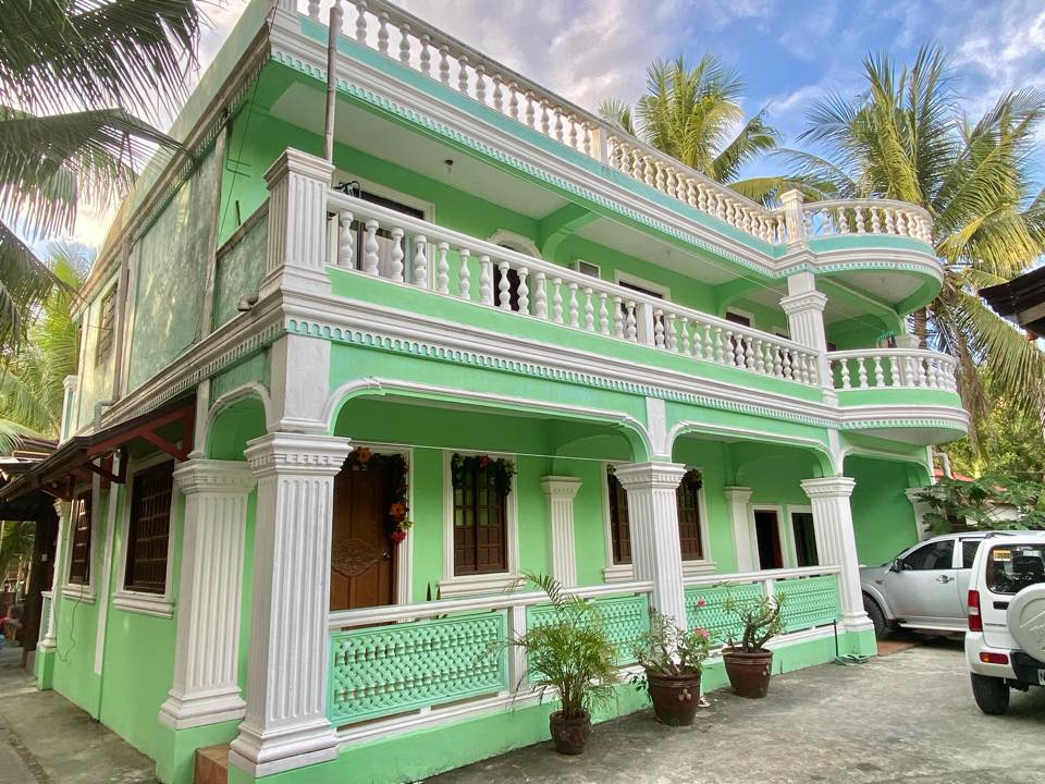 Jotikashe Beach House main building — green two-storey house with white colonial balustrades surrounded by palm trees